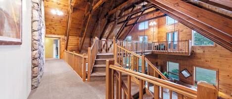 A wooden interior with a staircase leading to an upper level, stone wall on the left, and large windows on the right.