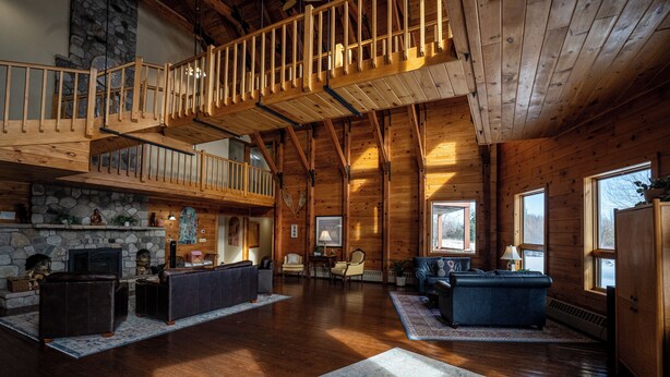 A spacious living area with a stone fireplace, wooden flooring, and a loft with a wooden railing.