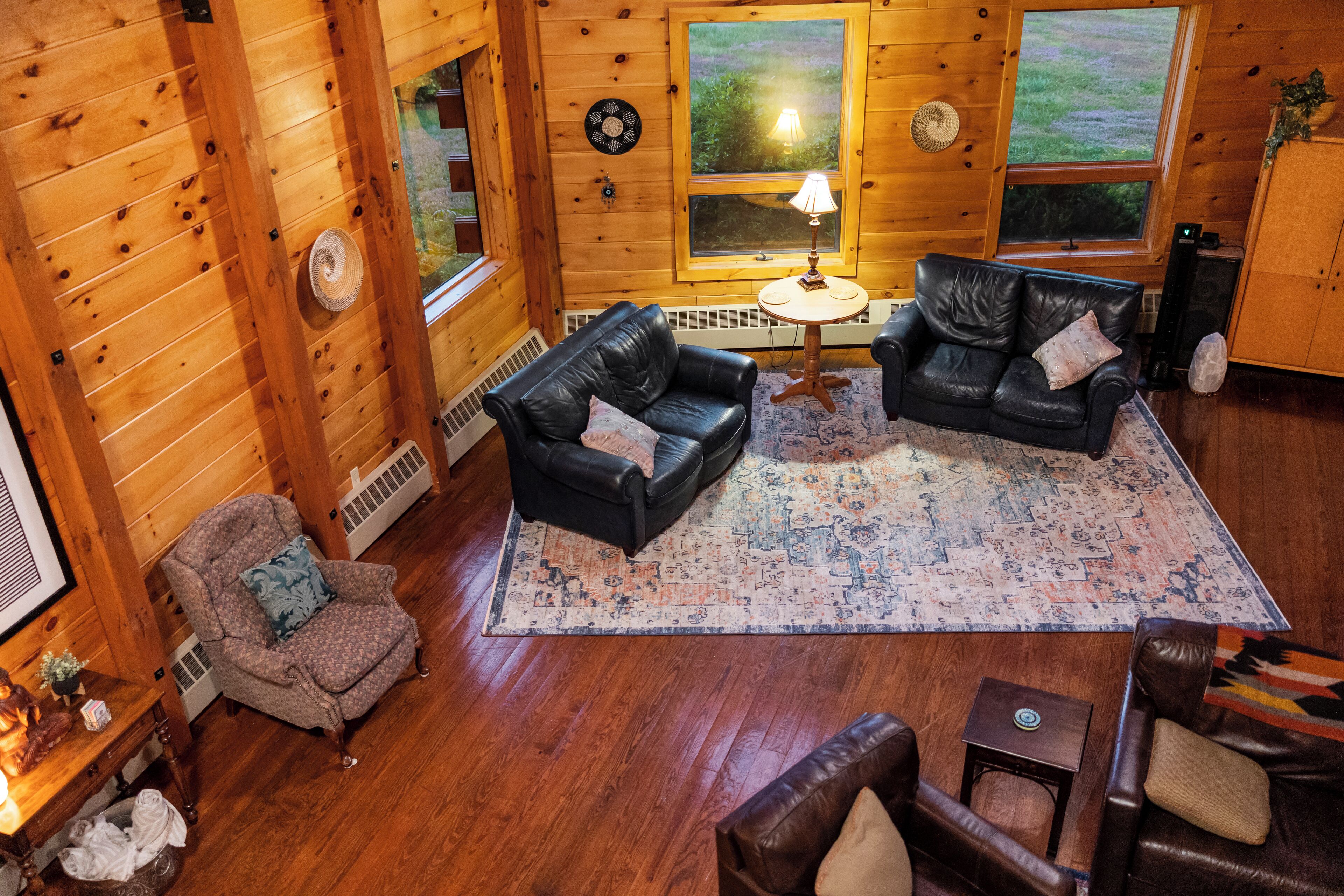 A cozy cabin interior with wooden walls, a black leather sofa, a patterned rug, and a small round table with a lamp.