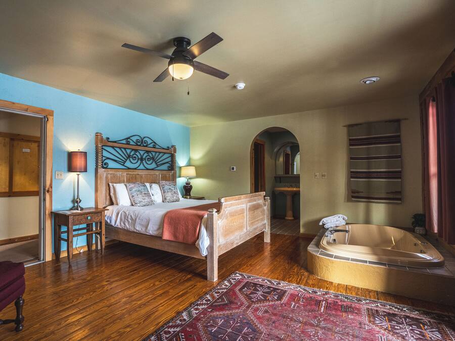 A bedroom with a wooden bed, a red armchair, a large window, a ceiling fan, and a bathtub.