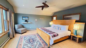 A bedroom with a large bed, a ceiling fan, a nightstand with a lamp, a chair, and a decorative rug.