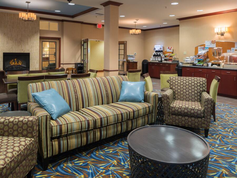 A hotel lobby with a sofa, armchairs, a coffee station, and a fireplace.