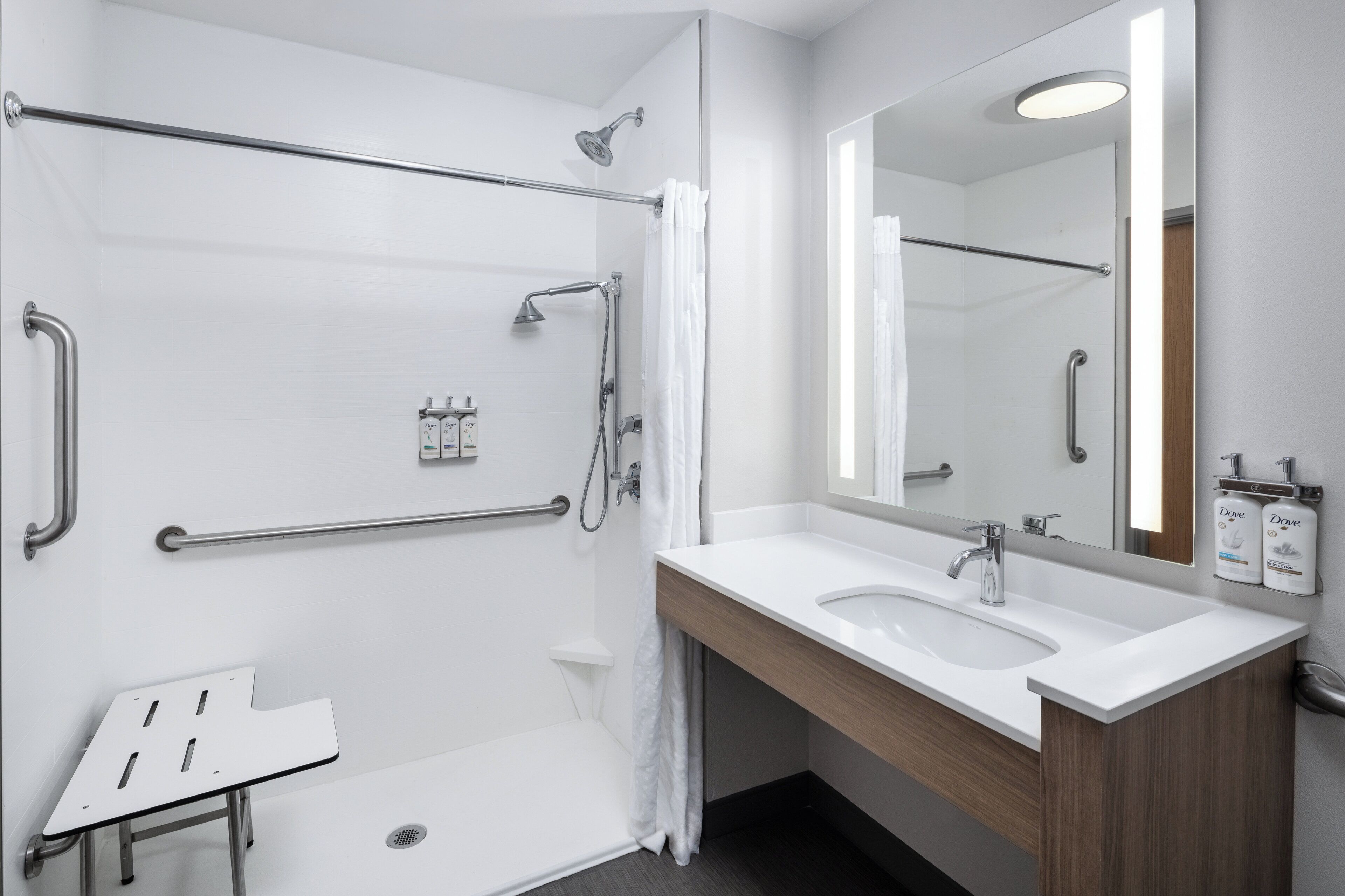 A modern bathroom with a shower, grab bars, a sink, and a mirror.