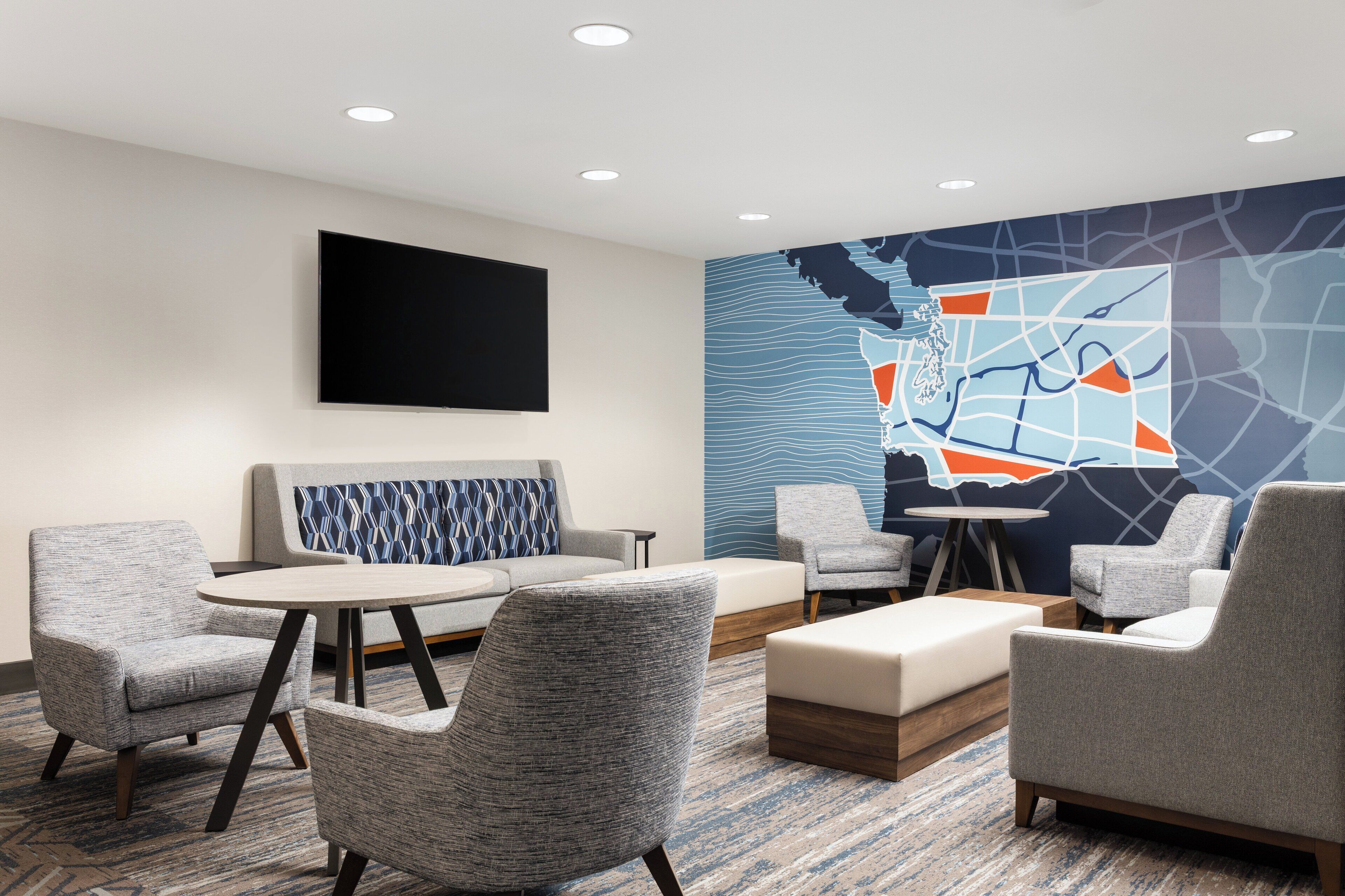 A modern hotel room with a large wall map, comfortable seating, and a flat-screen TV.