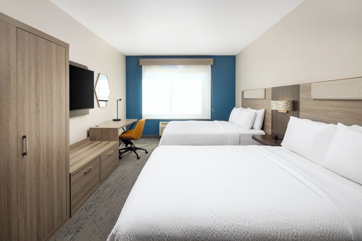 A hotel room with two beds, a desk, a chair, a TV, and a window.