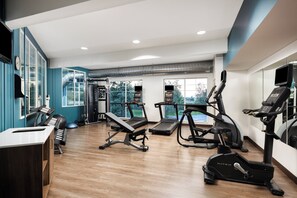 A modern gym with cardio machines, weight benches, and a large window offering a view of greenery. - Holiday Inn Express Hotel & Suites NORTH SEQUIM by IHG (Sequim)