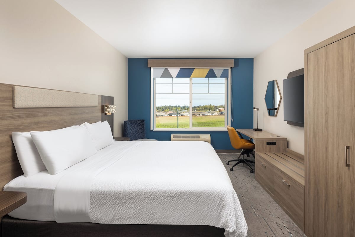 Ein Hotelzimmer mit einem großen Bett, einem Schreibtisch, einem Stuhl, einem Kleiderschrank und einem Fernseher.