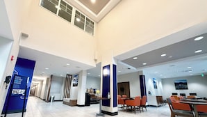A spacious hotel lobby with a high ceiling, multiple seating areas, and a reception desk.