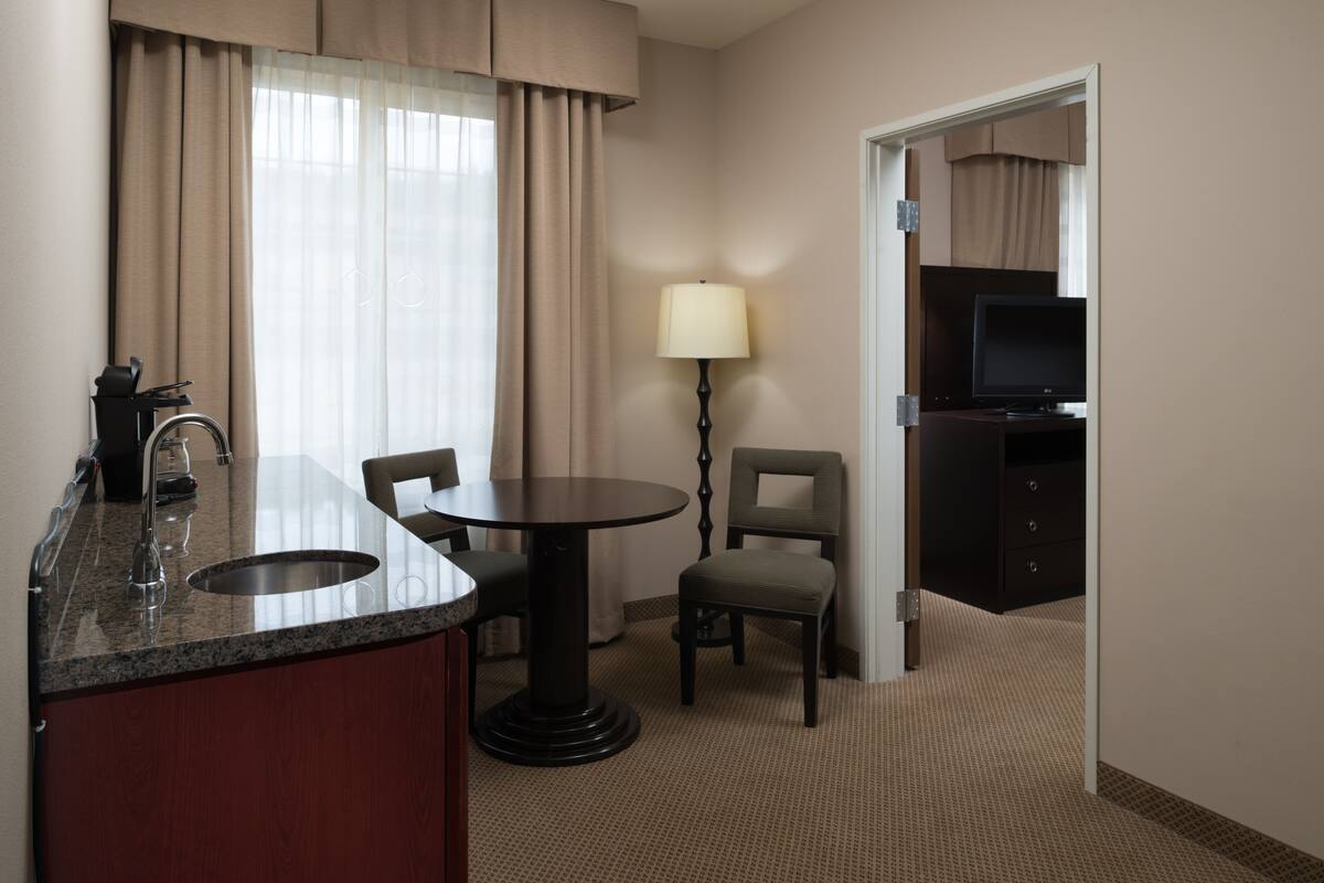 Ein Hotelzimmer mit Küchenzeile, einem Essbereich mit Tisch und Stühlen, einer Lampe und einem Fernseher.