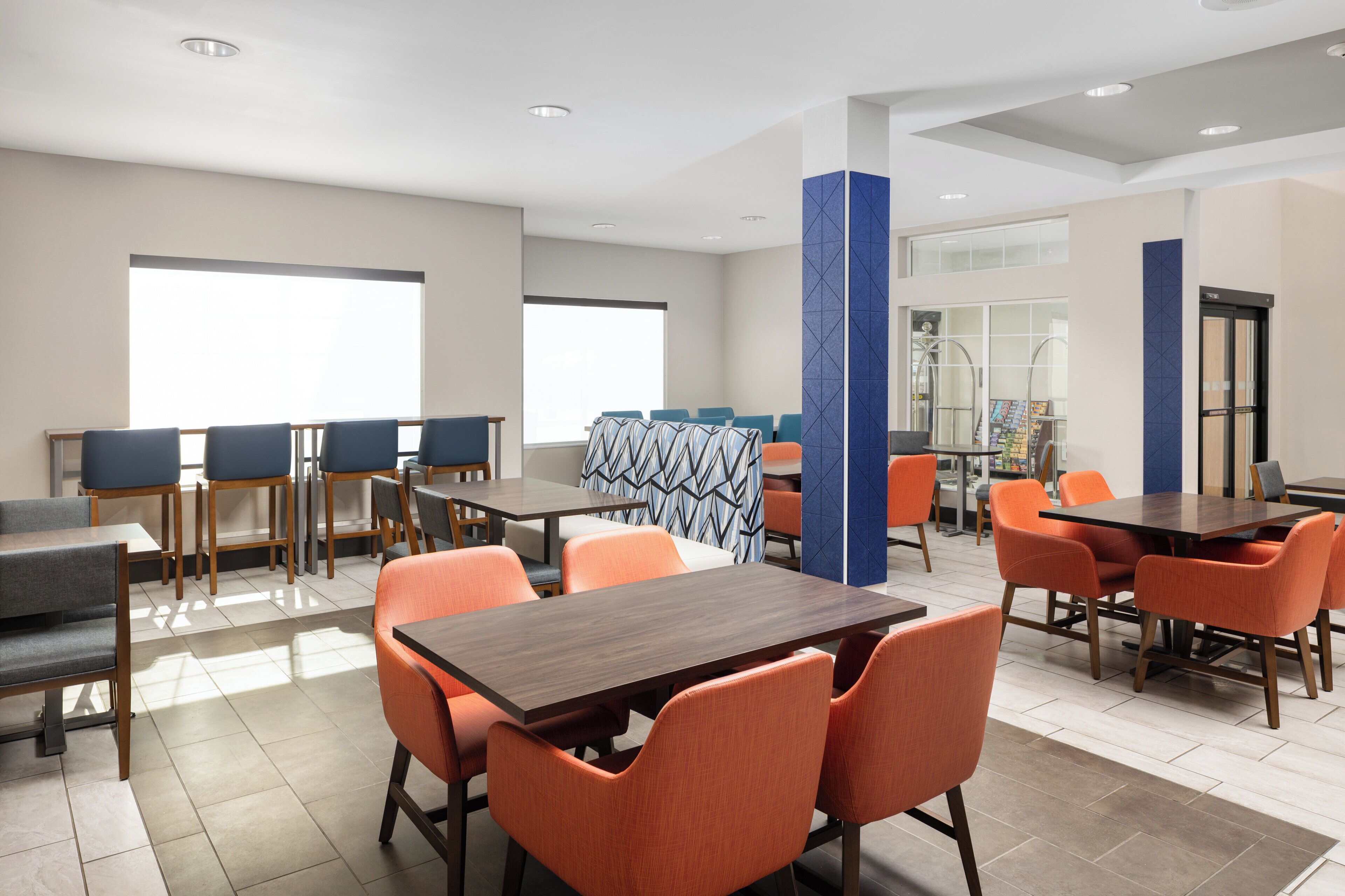 Un hall d’hôtel moderne doté de plusieurs espaces de détente, comprenant des tables et des chaises, ainsi que de grandes fenêtres laissant entrer la lumière naturelle.