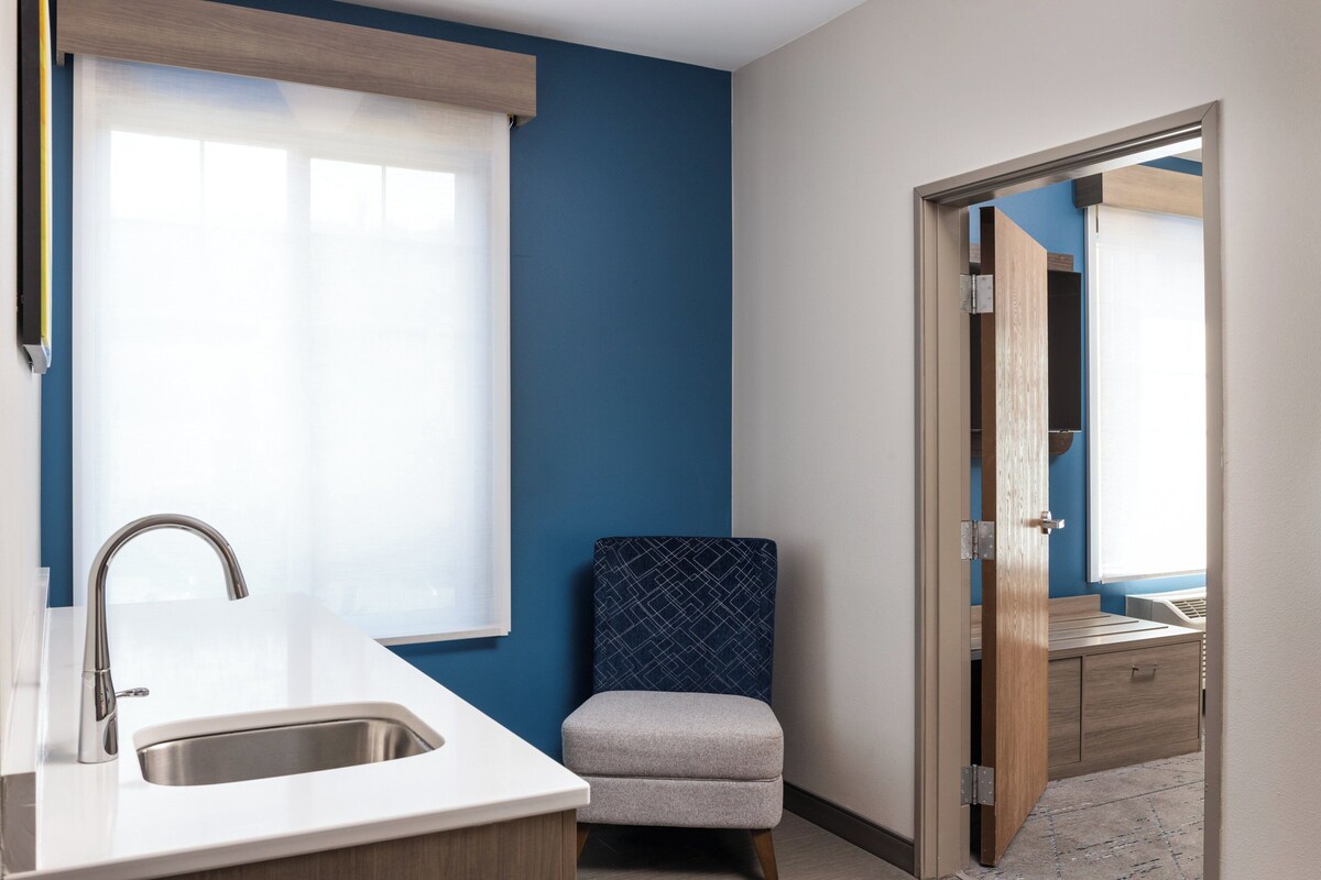 A modern bathroom with a sink, a chair, and a wooden cabinet.