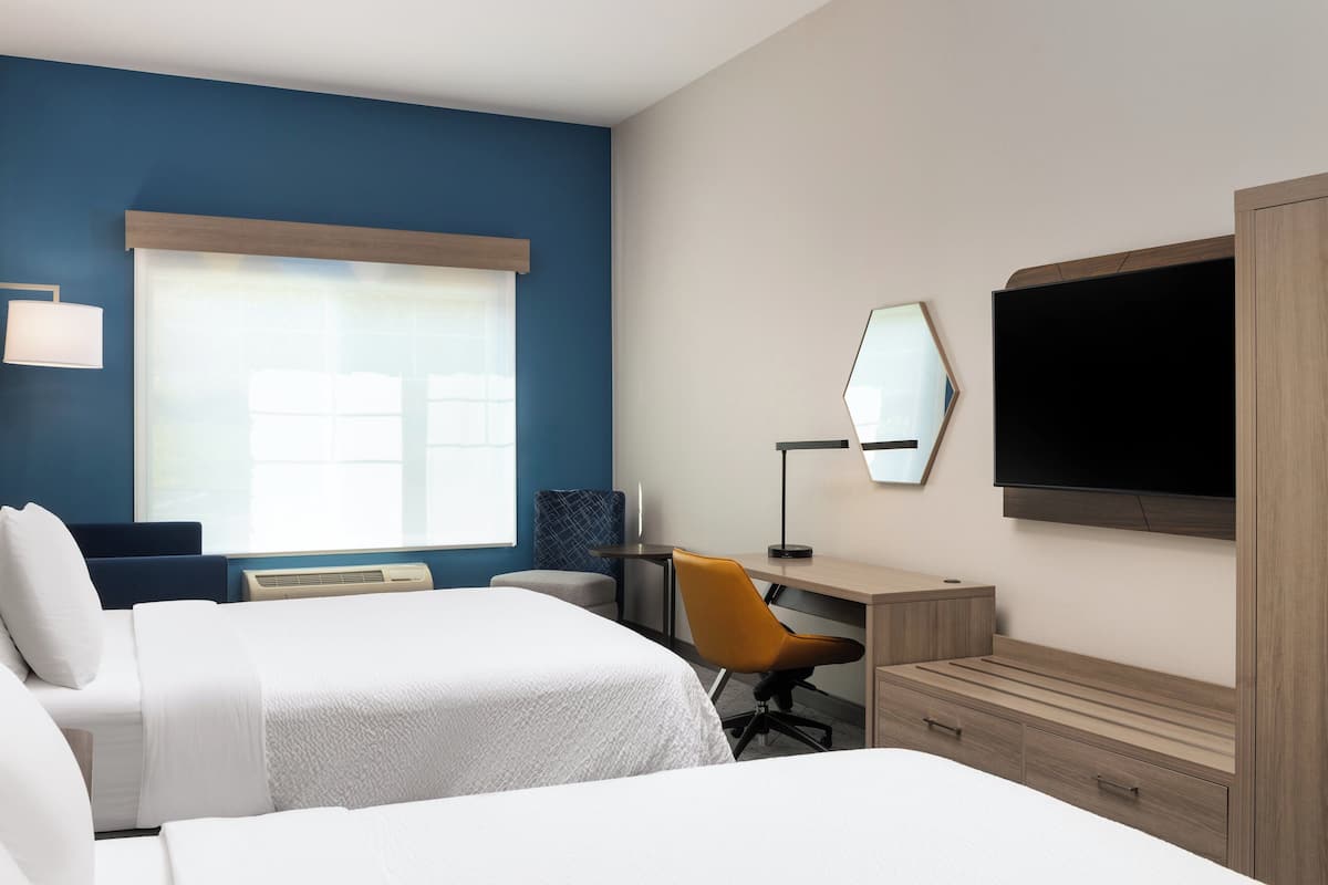 Ein Hotelzimmer mit zwei Betten, einem Schreibtisch, einem Stuhl, einem Fernseher und einem großen Fenster.