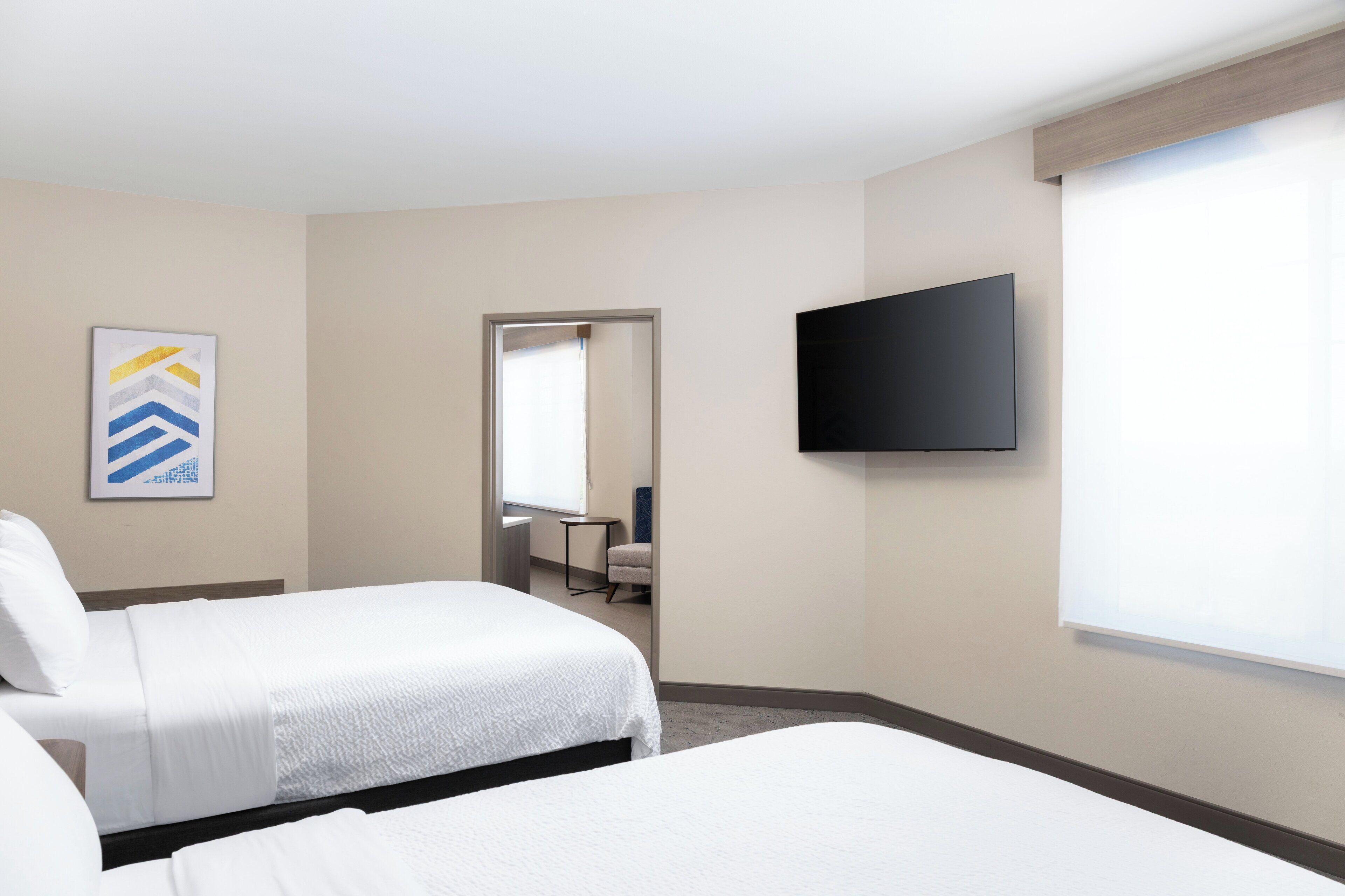 A hotel room with two beds, a flat-screen TV mounted on the wall, a window, and a door leading to a bathroom.