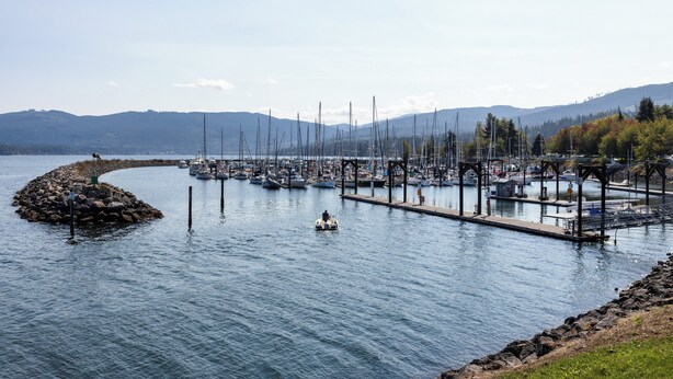 A marina with boats docked, a small island, and mountains in the background.