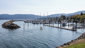 A marina with boats docked, a small island, and mountains in the background.
