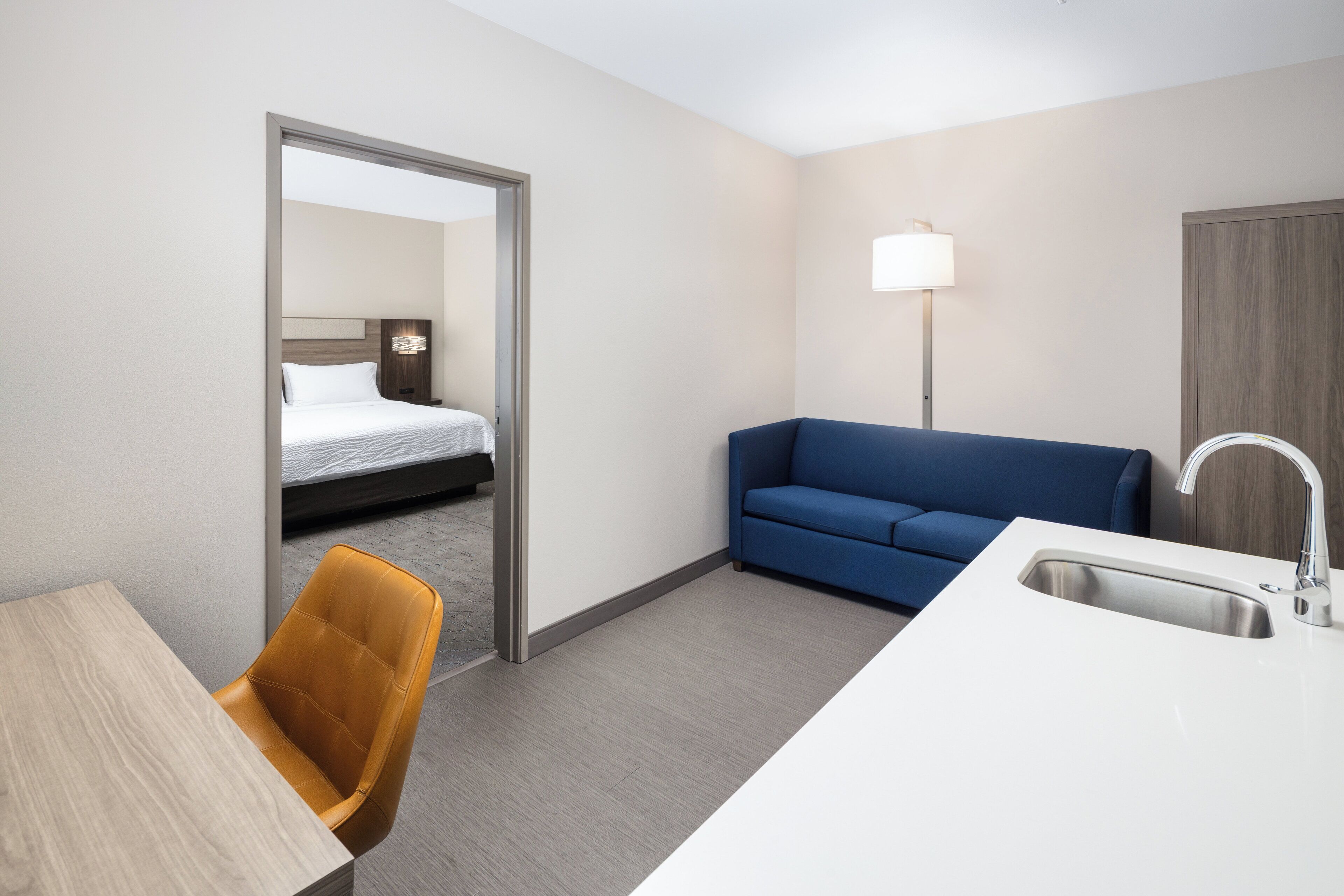 Una habitación de hotel con una cama, un sofá azul, un escritorio con una silla y un lavamanos.