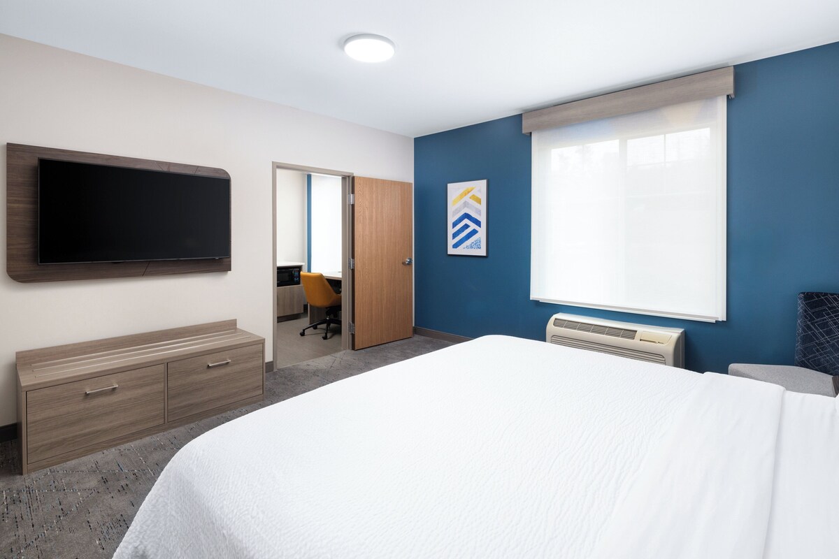 A hotel room with a bed, a TV mounted on the wall, a desk, and a chair.