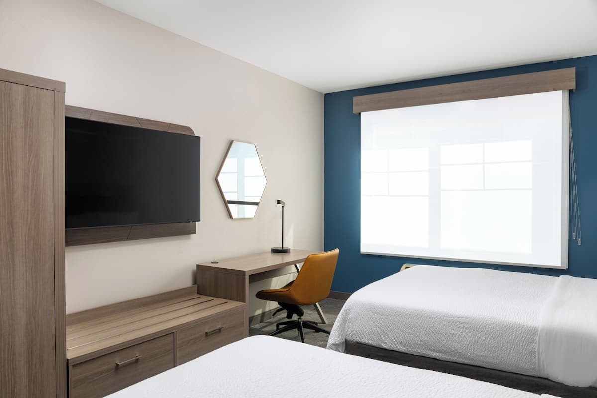 Ein Hotelzimmer mit einem Bett, einem Schreibtisch, einem Sessel, einem Fernseher und einem großen Fenster.