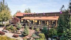 A building with a covered outdoor seating area, surrounded by landscaped gardens and trees.