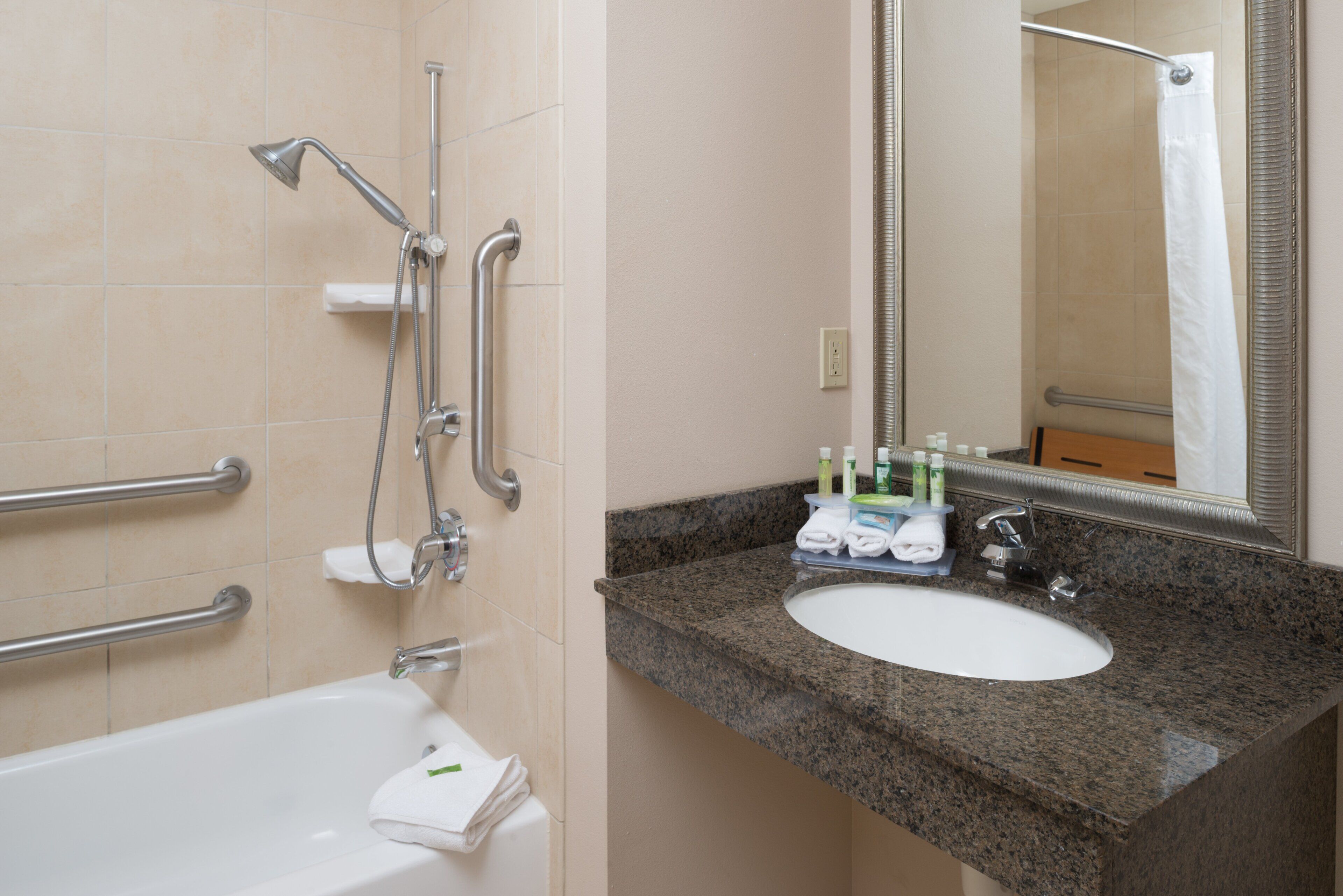 A bathroom with a bathtub, a sink with a granite countertop, and a mirror.