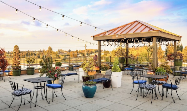 Une terrasse extérieure avec des tables et des chaises, un belvédère et des guirlandes lumineuses.