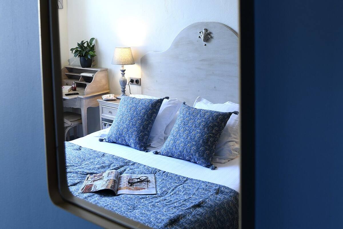 A bedroom with a bed, pillows, a nightstand, a lamp, and a wall-mounted mirror.