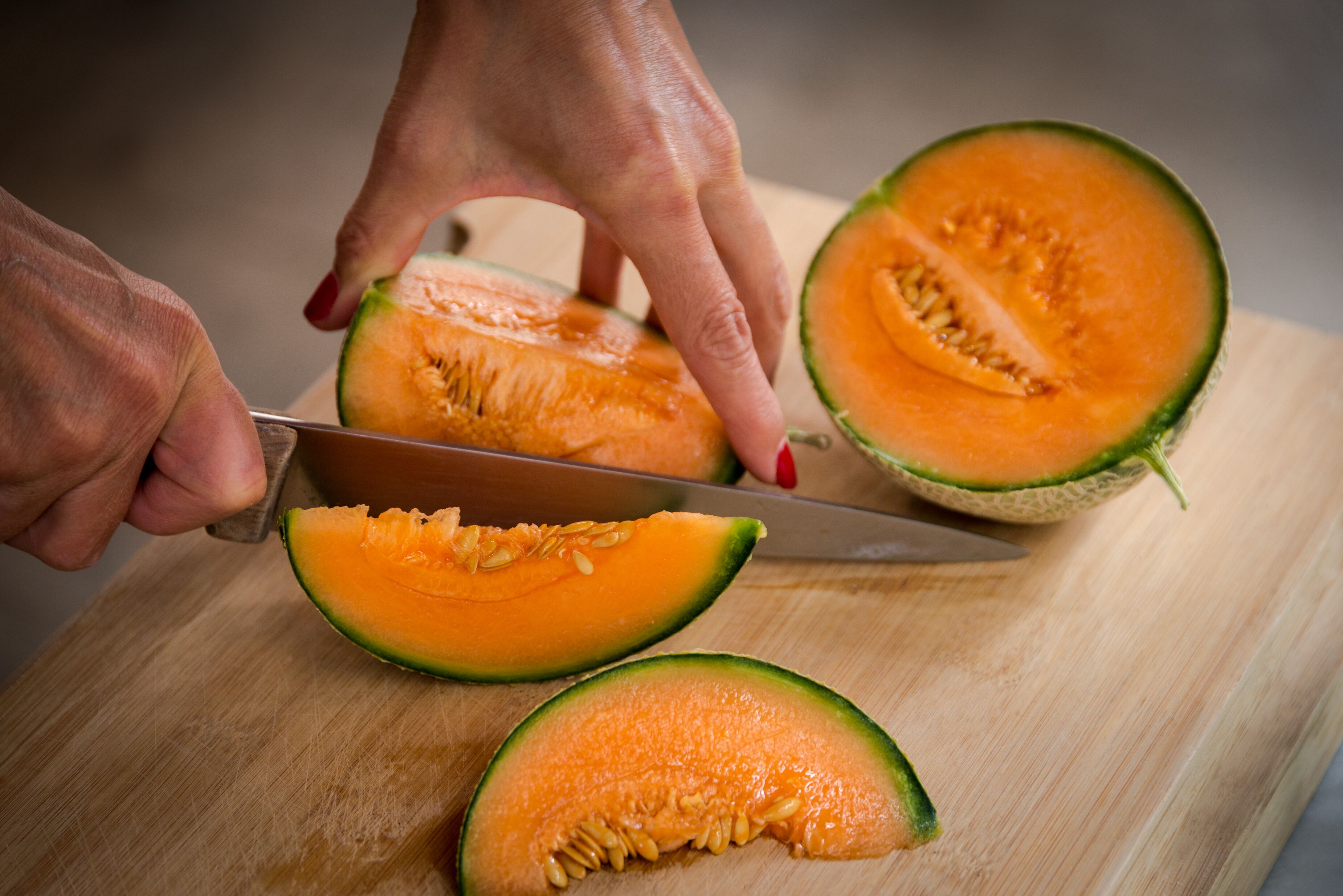 Una persona cortando un melón cantalupo sobre una tabla de madera.