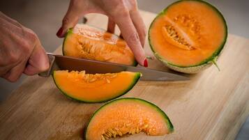 Una persona cortando un melón cantalupo sobre una tabla de madera.