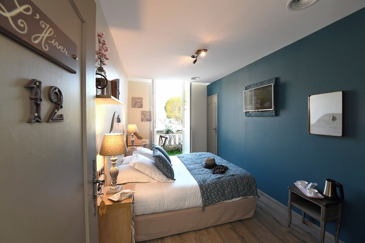Un dormitorio con cama, lámparas de noche, una mesita, televisor y ventana con vistas al exterior.