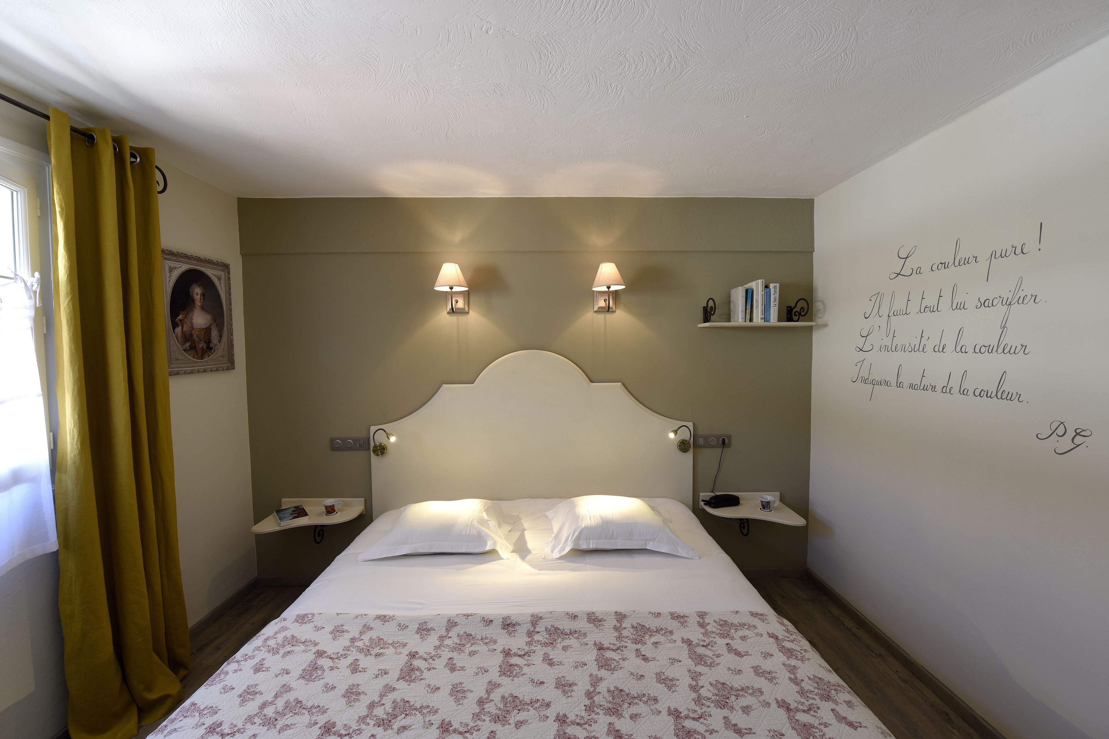 Un dormitorio con cama, dos mesitas de noche, una mesita auxiliar, un estante en la pared y una ventana con cortinas.