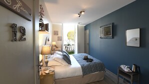 Un dormitorio con cama, lámparas de noche, una mesita, televisor y ventana con vistas al exterior.