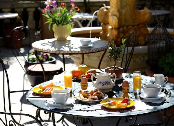 Ein runder Metalltisch mit Frühstücksangeboten, darunter Croissants, Obst und Kaffee.