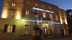 Un hotel histórico con fachada clásica, una entrada central y una esquina de calle bien iluminada.