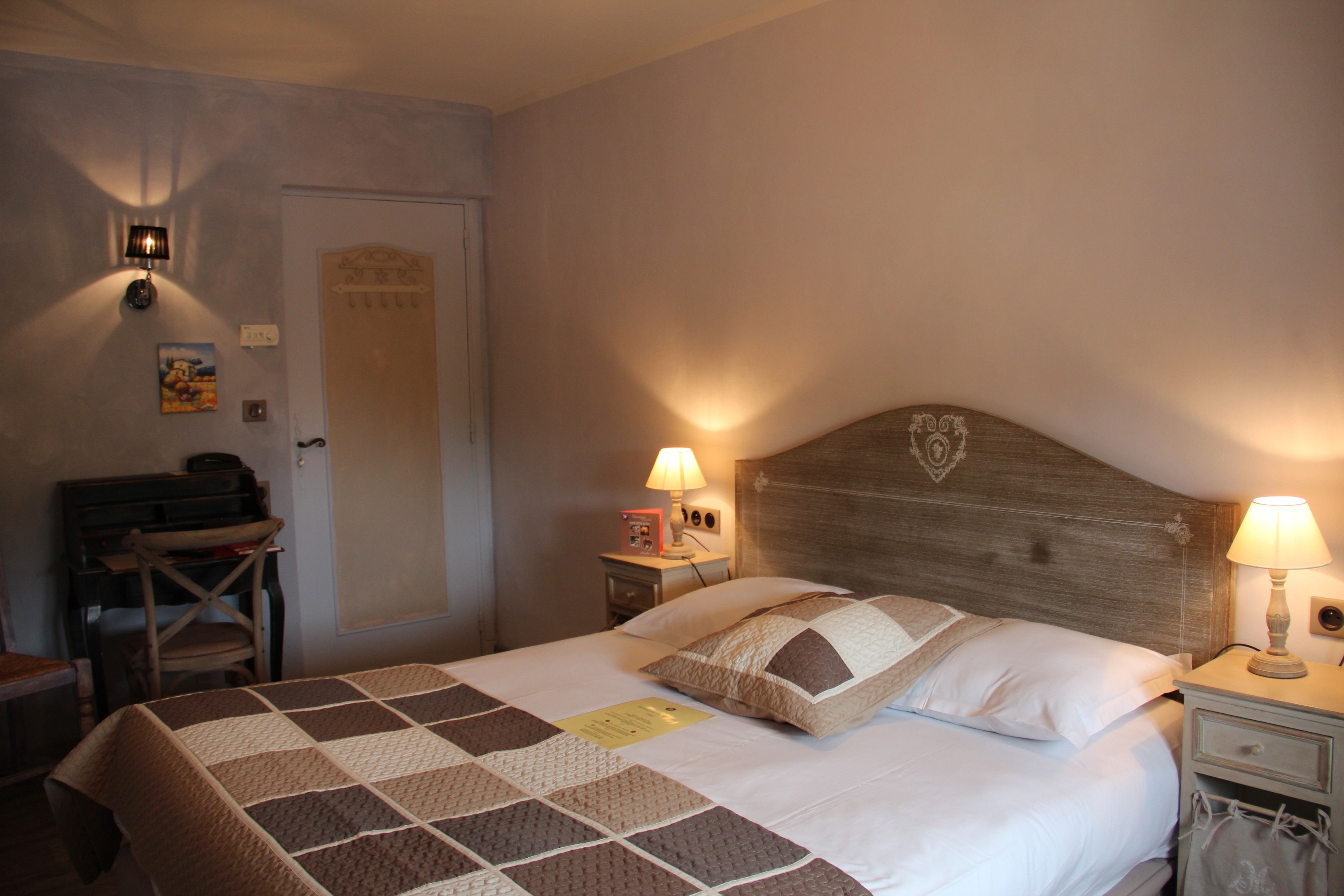 A neatly made bed with a checkered bedspread, a wooden headboard, two bedside lamps, and a small nightstand with a lamp.