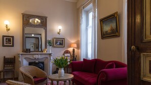 Una habitación tradicional con un sofá rojo, sillas de mimbre, chimenea y un espejo.
