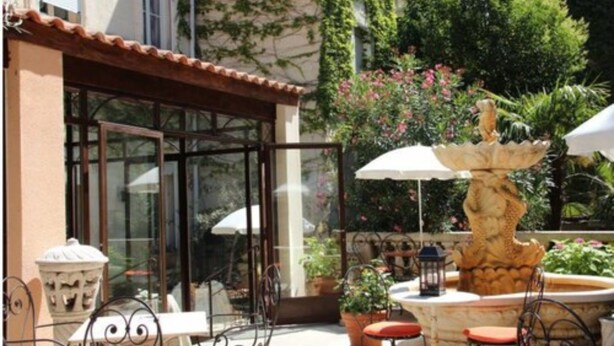 Un patio al aire libre con una fuente, mesas, sillas y plantas en macetas.