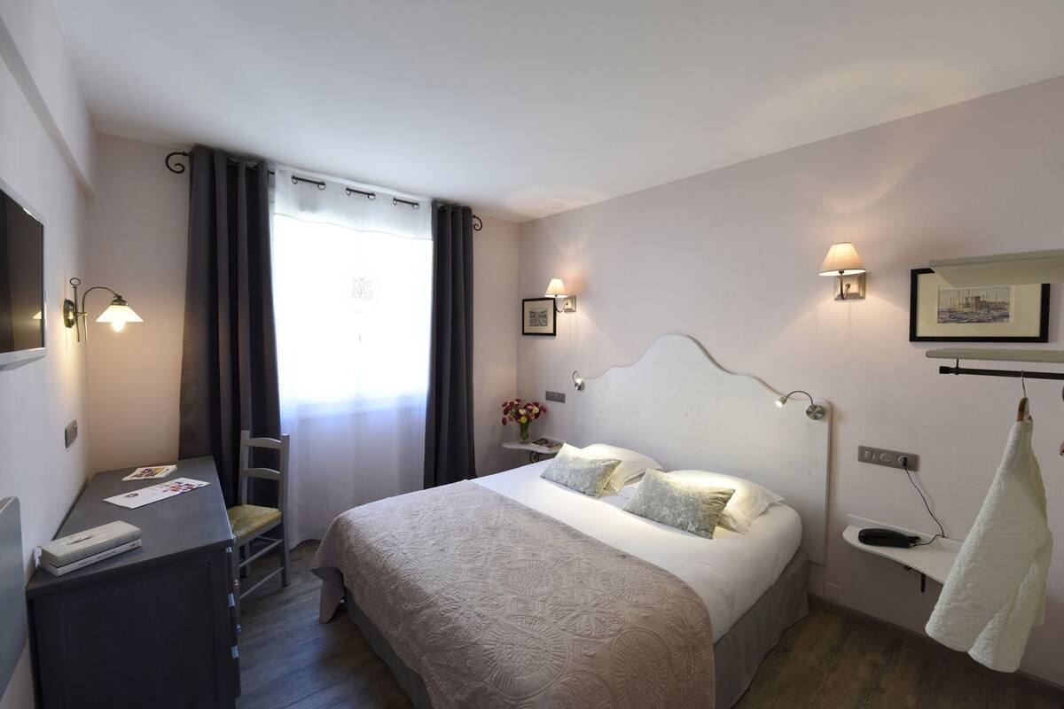 A bedroom with a bed, bedside lamps, a desk, a chair, a window with curtains, and a towel rack.