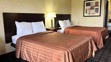 A hotel room with two beds, a nightstand with a lamp, a framed picture on the wall, and a carpeted floor.