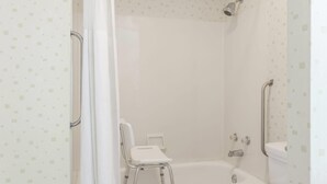 A shower with a handheld showerhead, a white chair, and a bathtub. - Travelodge by Wyndham Seymour (Seymour)