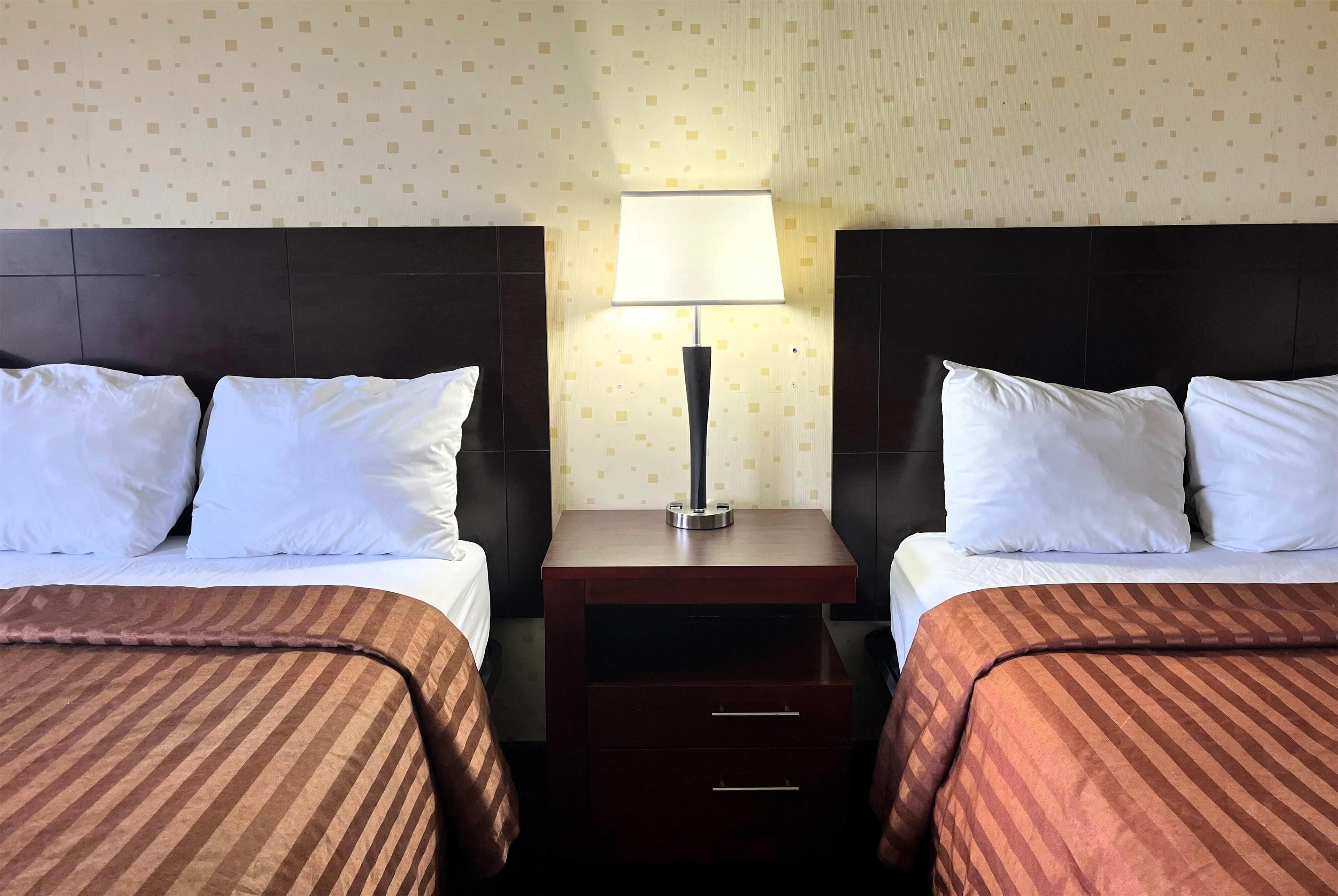 A hotel room with two beds, a nightstand with a lamp, and a patterned wall.