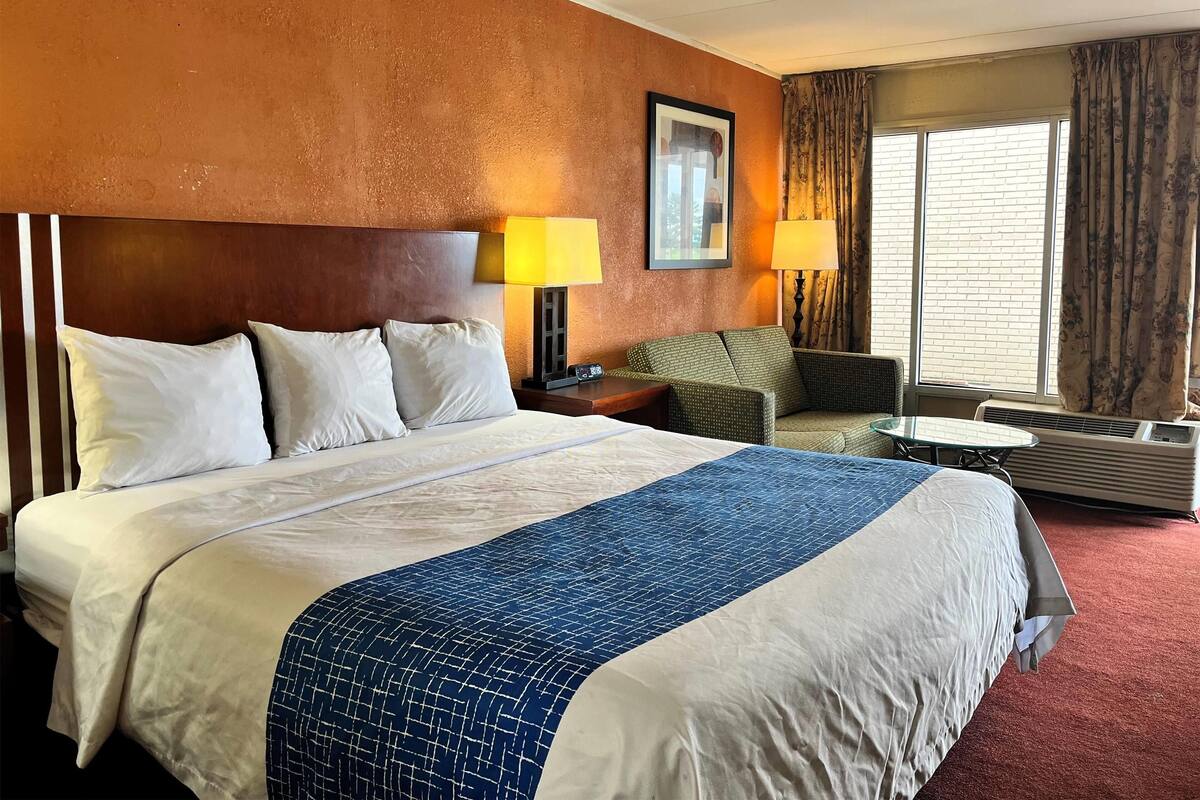 Ein Hotelzimmer mit einem großen Bett, zwei Nachttischlampen, einem kleinen Tisch, einer Couch und einem Fenster mit Vorhängen.