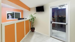A reception area with a counter, a potted plant, a television, and a sliding glass door. - Travelodge by Wyndham Seymour (Seymour)