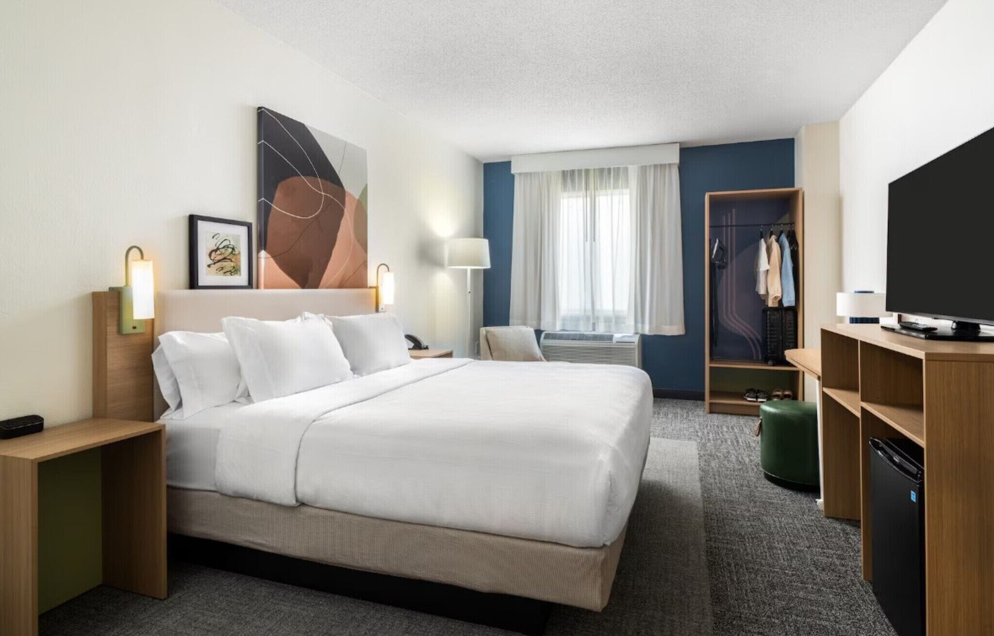 Une chambre d’hôtel comprenant un lit, des tables de chevet, une télévision, une armoire et une fenêtre avec des rideaux.