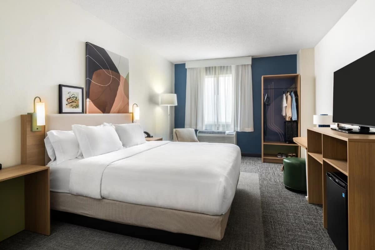 Een hotelkamer met een bed, nachtkastjes, een televisie, een kledingkast en een raam met gordijnen.