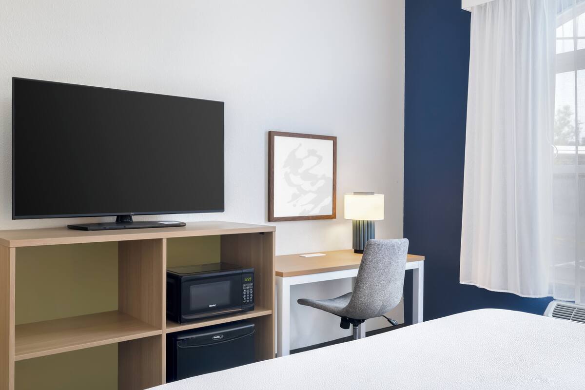 Een hotelkamer met een bed, een bureau met computer, een televisie, een magnetron en een stoel.