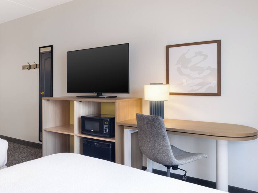 A hotel room with a bed, a desk with a chair, a television, a microwave, and a small refrigerator.