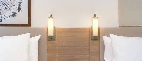 Habitación de hotel con dos camas, una mesita de noche de madera y dos luces fijadas a la pared.
