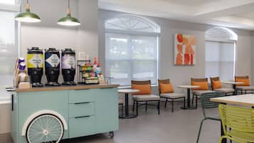 Een café met een blauwgroene kar, meerdere koffieautomaten en een groot raam met uitzicht.