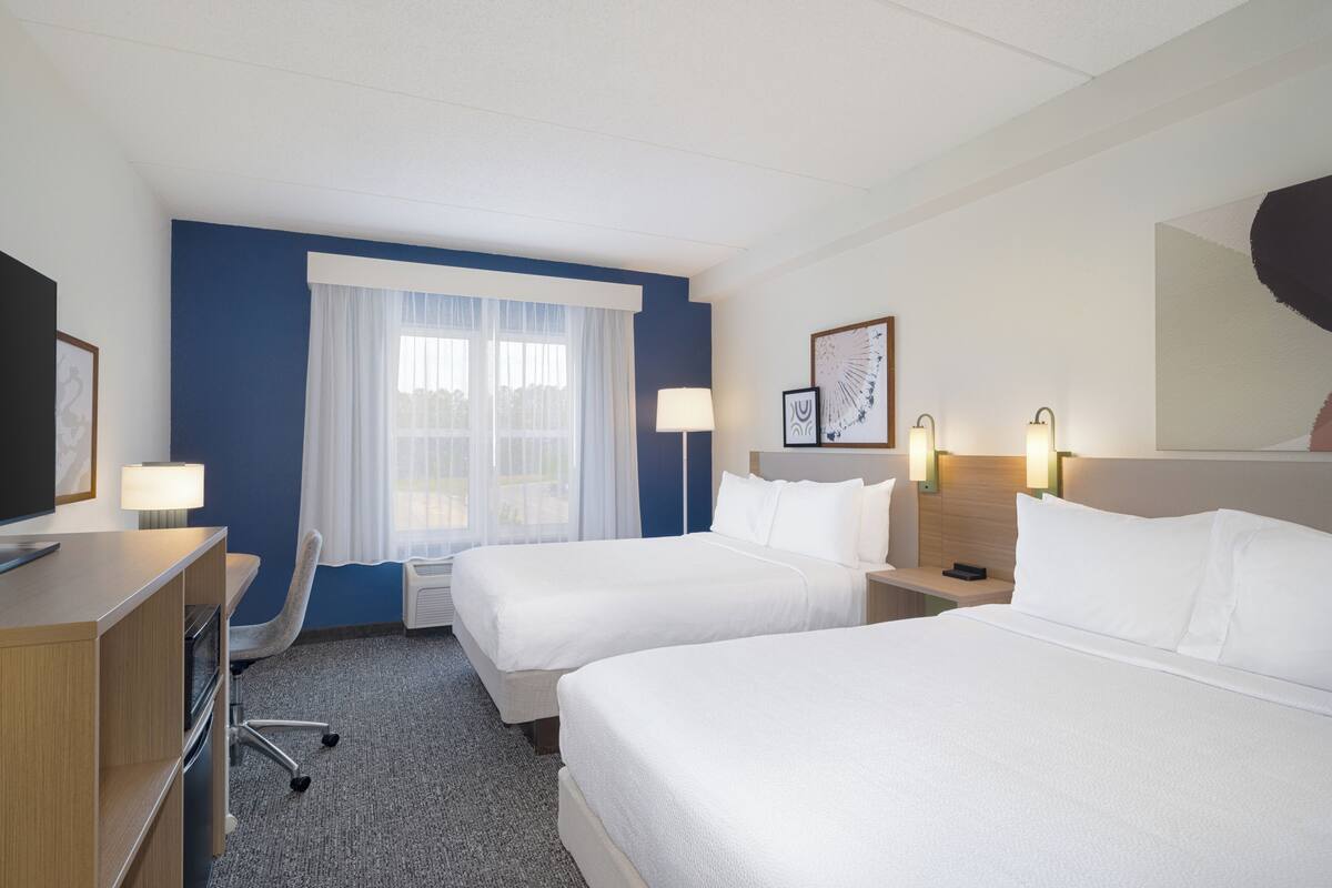 Een hotelkamer met twee bedden, een bureau, een stoel, een televisie en een raam met gordijnen.