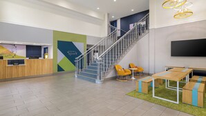 A hotel lobby with a reception desk, a staircase, seating area, and a flat-screen TV.